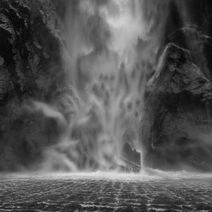 Black and white fine art photography print of a dramatic Milford Sound waterfall cascading over ancient rock with ghostly mist figures emerging from the spray