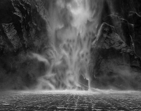 Black and white fine art photography print of a dramatic Milford Sound waterfall cascading over ancient rock with ghostly mist figures emerging from the spray