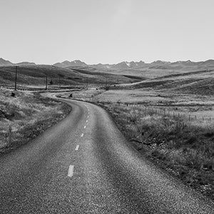 Black and white fine art photography print of a winding road through rolling hills near Wanaka New Zealand with distant mountain ranges